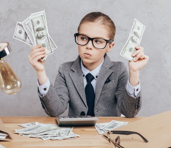 Child at a desk holding wads of cash tries to understand the cost of tooth extractions