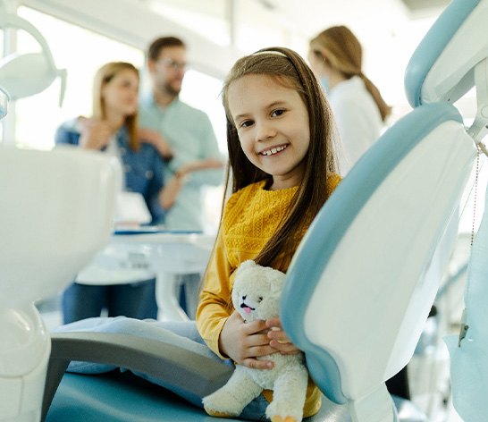 Child smiling while holding stuffed animal in treatment chair