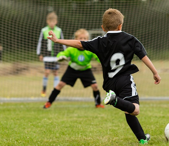 Child kicking soccer ball into net