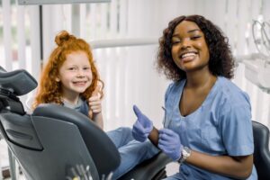 a pediatric dentist smiling and giving a thumbs-up with a patient